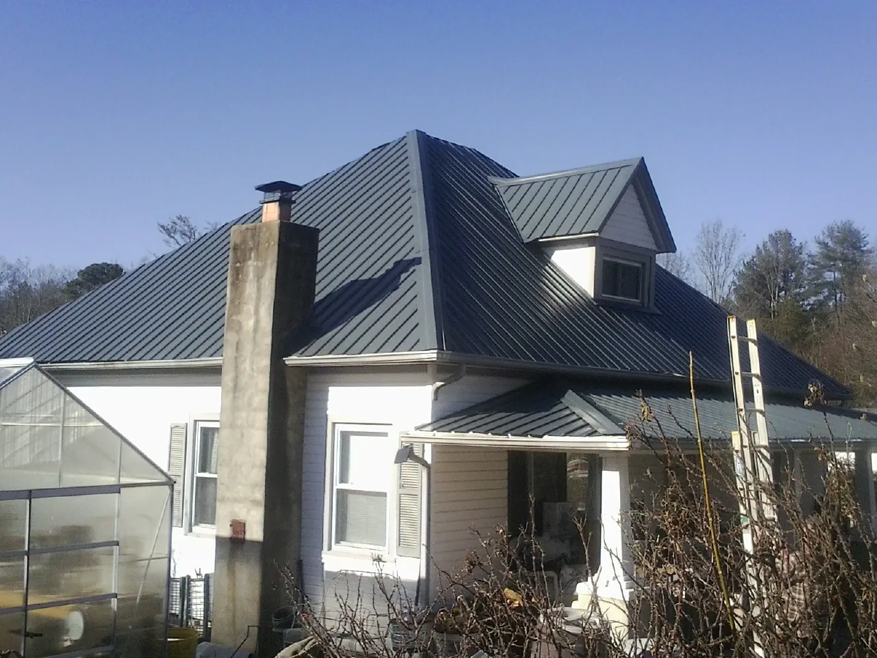 Dark blue standing seam metal roof on a white farmhouse with dormer — Slate & Tile Roof Repair by Roofing Brothers in Wingate
